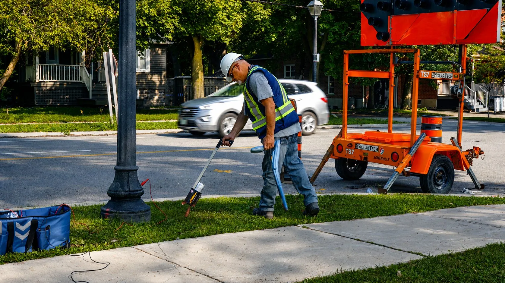 Utility locator scanning a boulevard beside a traffic control trailer